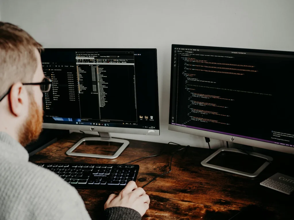 Software developer writing code across two monitors